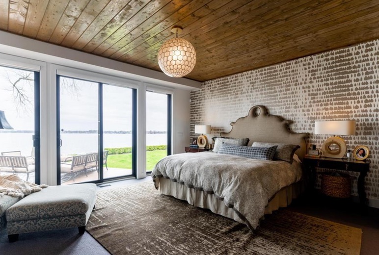 Layered lakefront primary bedroom with a wood ceiling and patterned wall