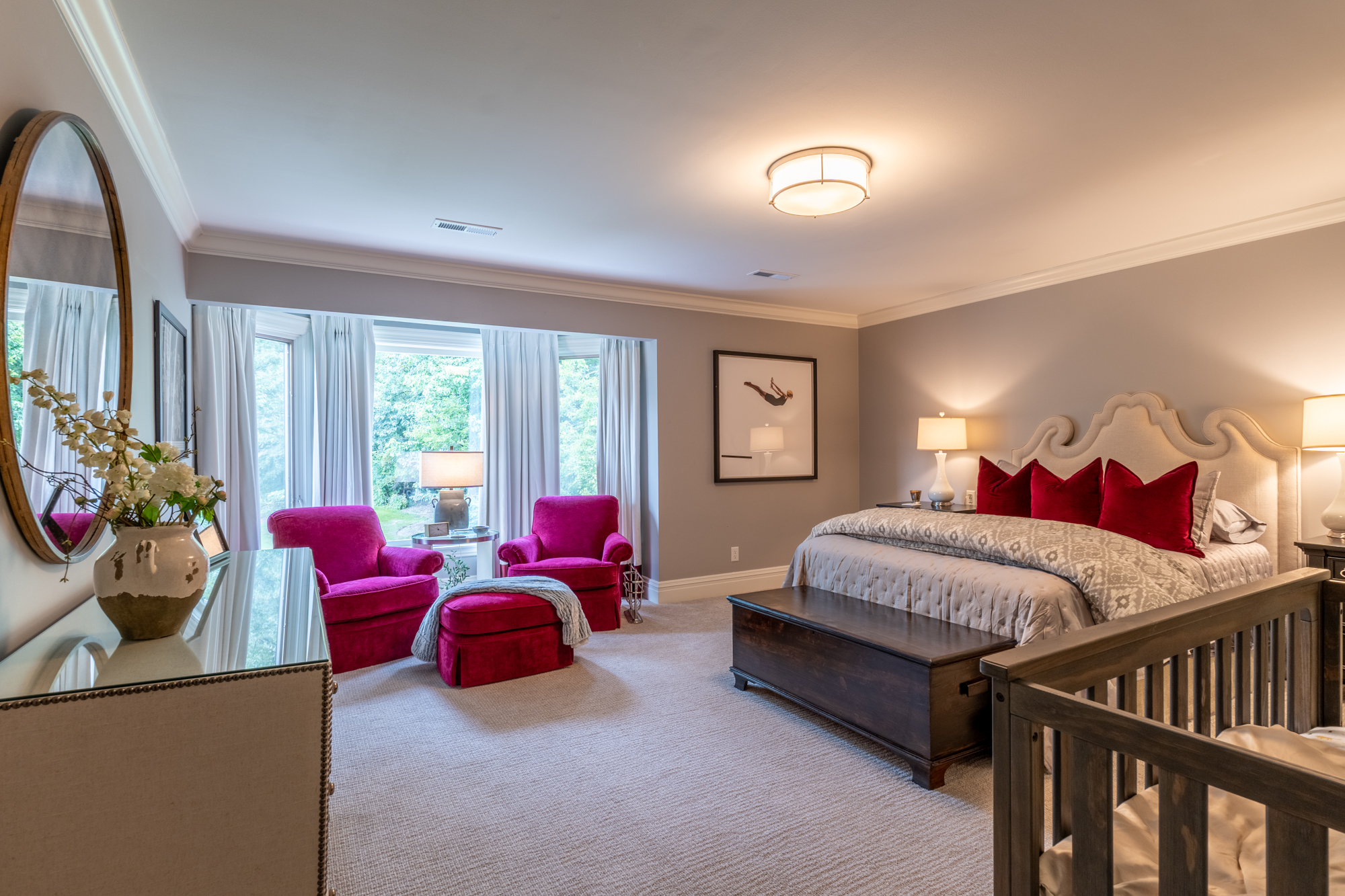 Primary bedroom with a sculptural upholstered bed and vivid raspberry seating